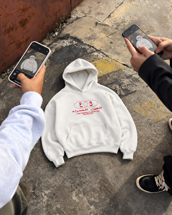 The Red Eye Hoodie in white — flat-lay front view photographed on phones